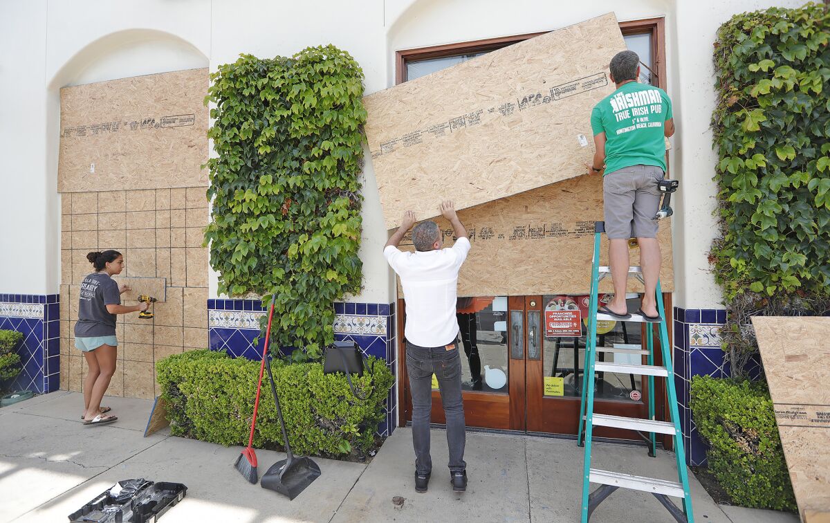 Business owners Tamer Yleizet, center, and Ray Hartnett, right, remove plywood panels on Monday that protected their storefronts from vandalism and looters during Sunday's protest in downtown Huntington Beach. Yleizet owns the Cold Stone Creamery and Hartnett the Irishman bar.