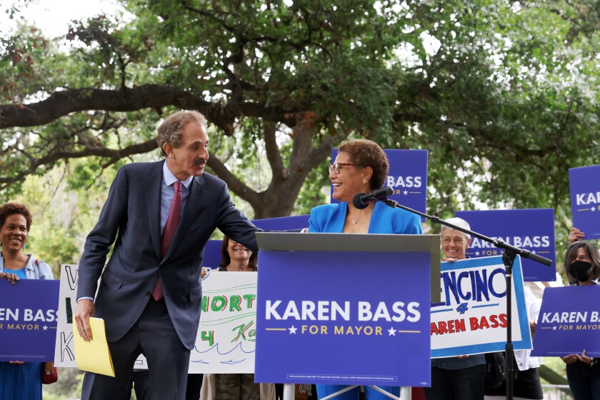 Karen Bass, at the microphone, turns to speak to Mike Feuer at an event in a park.