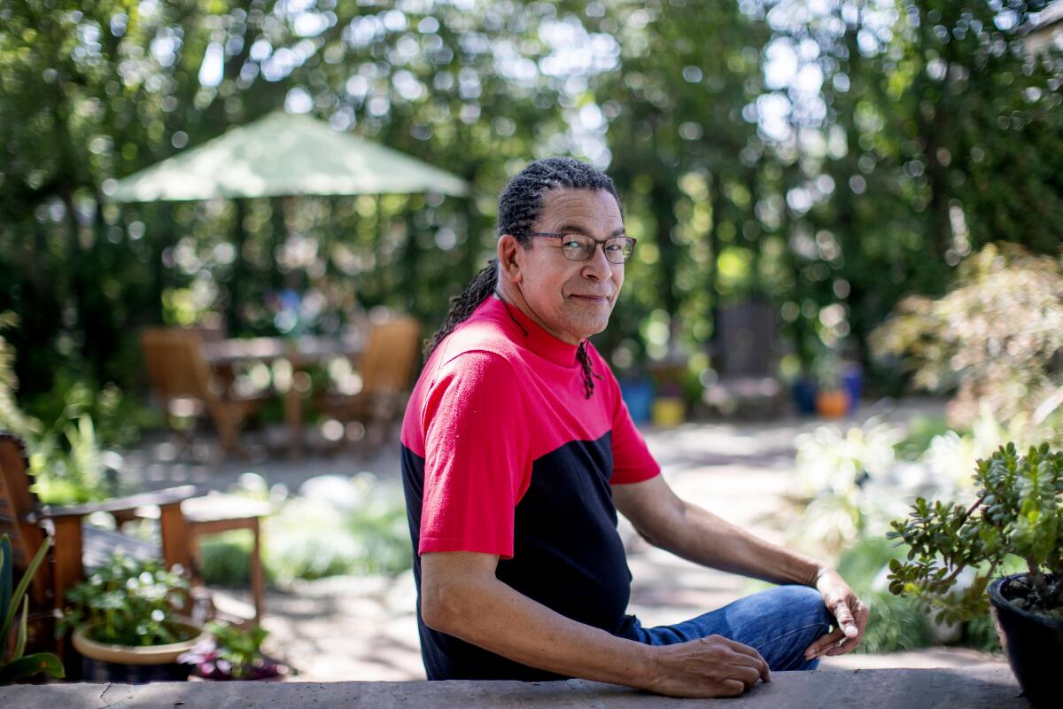 Mark Steven Greenfield sits on a patio in his tree-lined garden