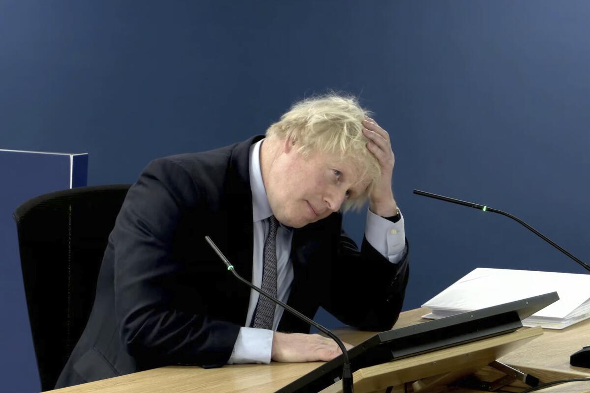 Boris Johnson sits at a microphone with his head rested on one hand.
