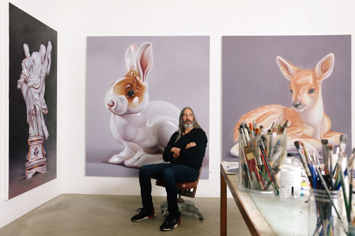 Artist Robert Russell stands in his art studio by his giant paintings of tiny porcelain animal figurines.