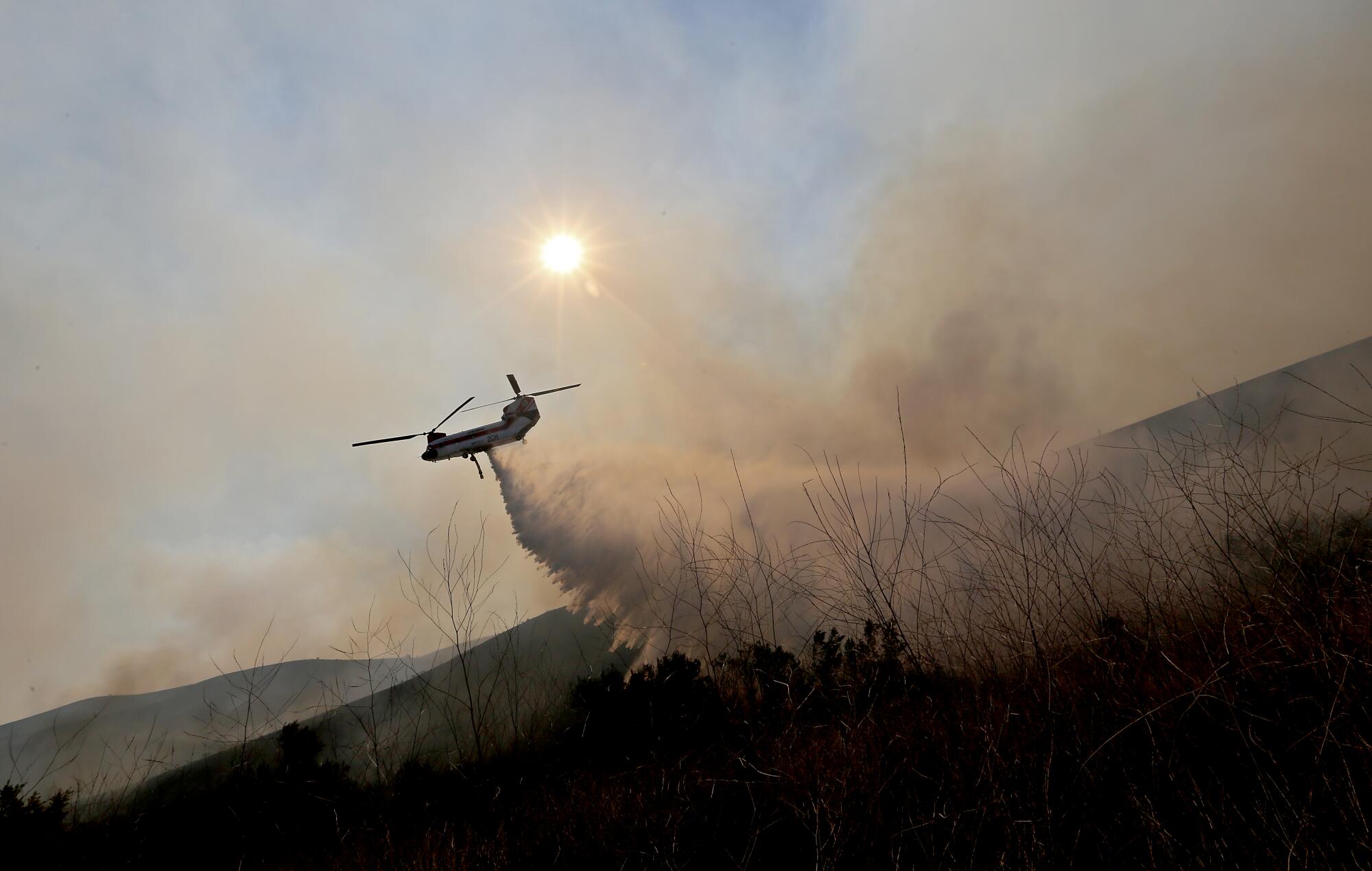 A helicopter drops water amid smoke