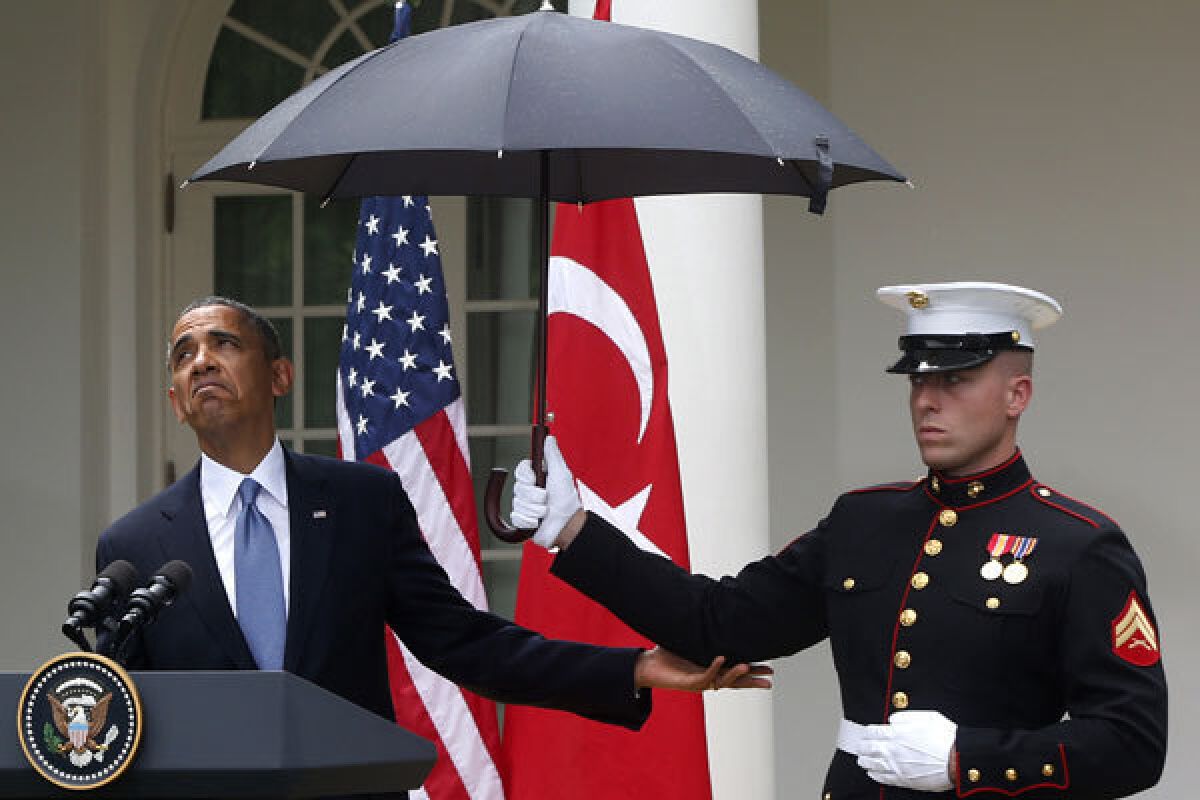 President Obama looks to see whether it is still raining as a Marine holds an umbrella for him during a news conference.