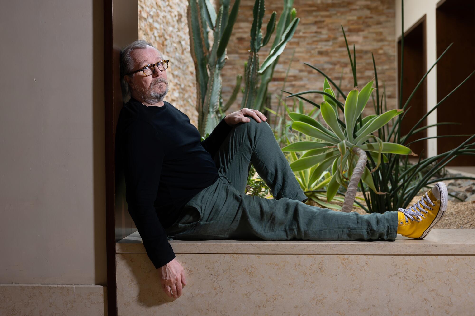 Gary Oldman stretches out along an outdoor planter for a portrait.