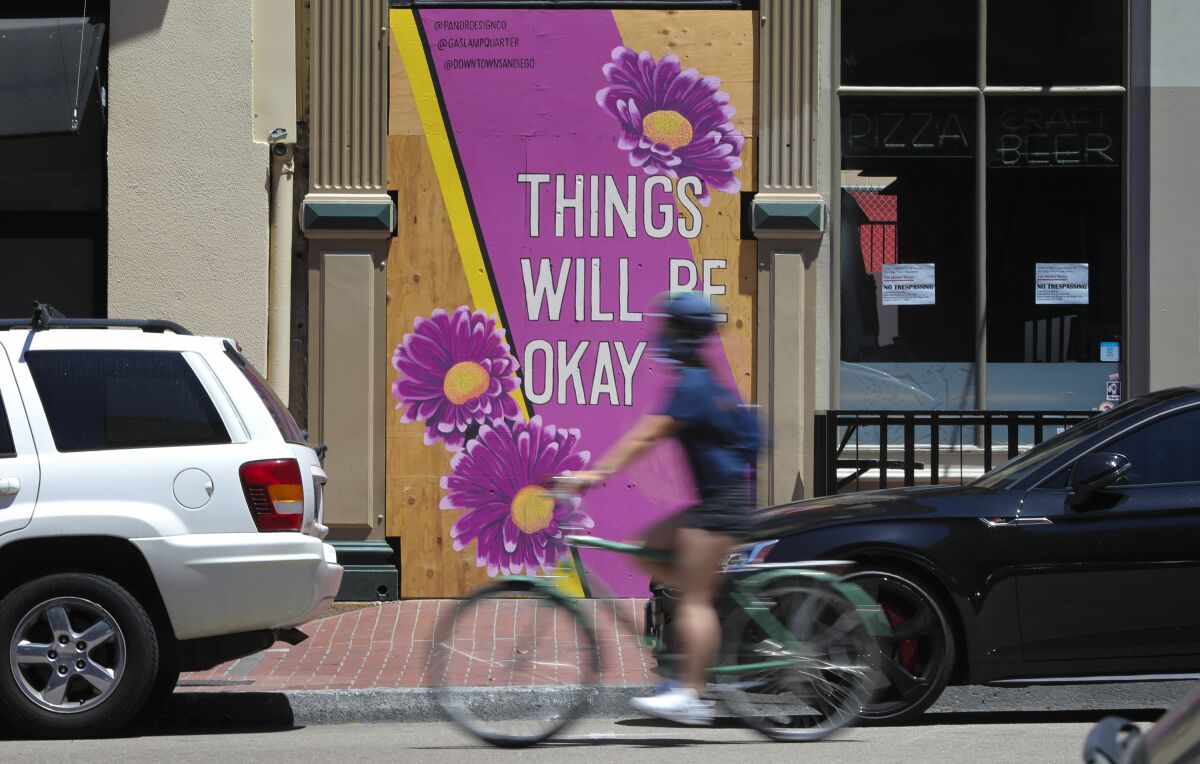A cyclist passes a temporary mural on the doorway of Bang Bang, at 536 Market St. in downtown San Diego's Gaslamp Quarter, on May 21, 2020.