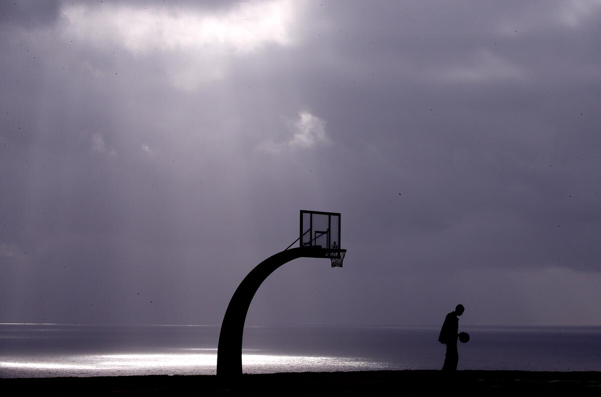 A lone man sits near a coastal basketball court.
