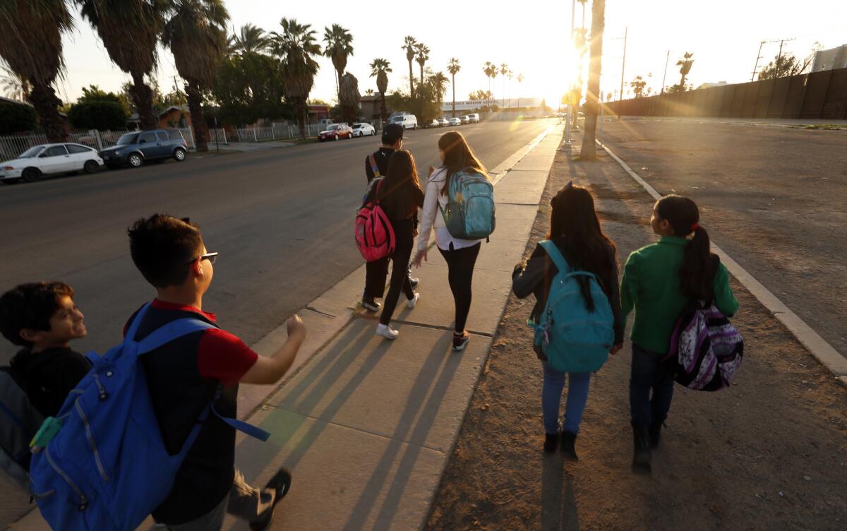 Izquierda: Después de cruzar la frontera desde Mexicali, México, los estudiantes se dirigen a la escuela por una acera paralela a la valla fronteriza (derecha), en Caléxico, California. Derecha: Calexico Mission School vista desde México, enmarcada por una porción de la cerca que limita California y México.