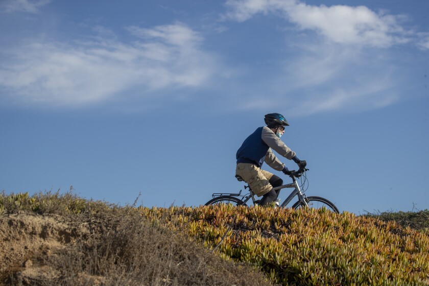 A man wears a mask while riding a bike in Huntington Beach on Monday.