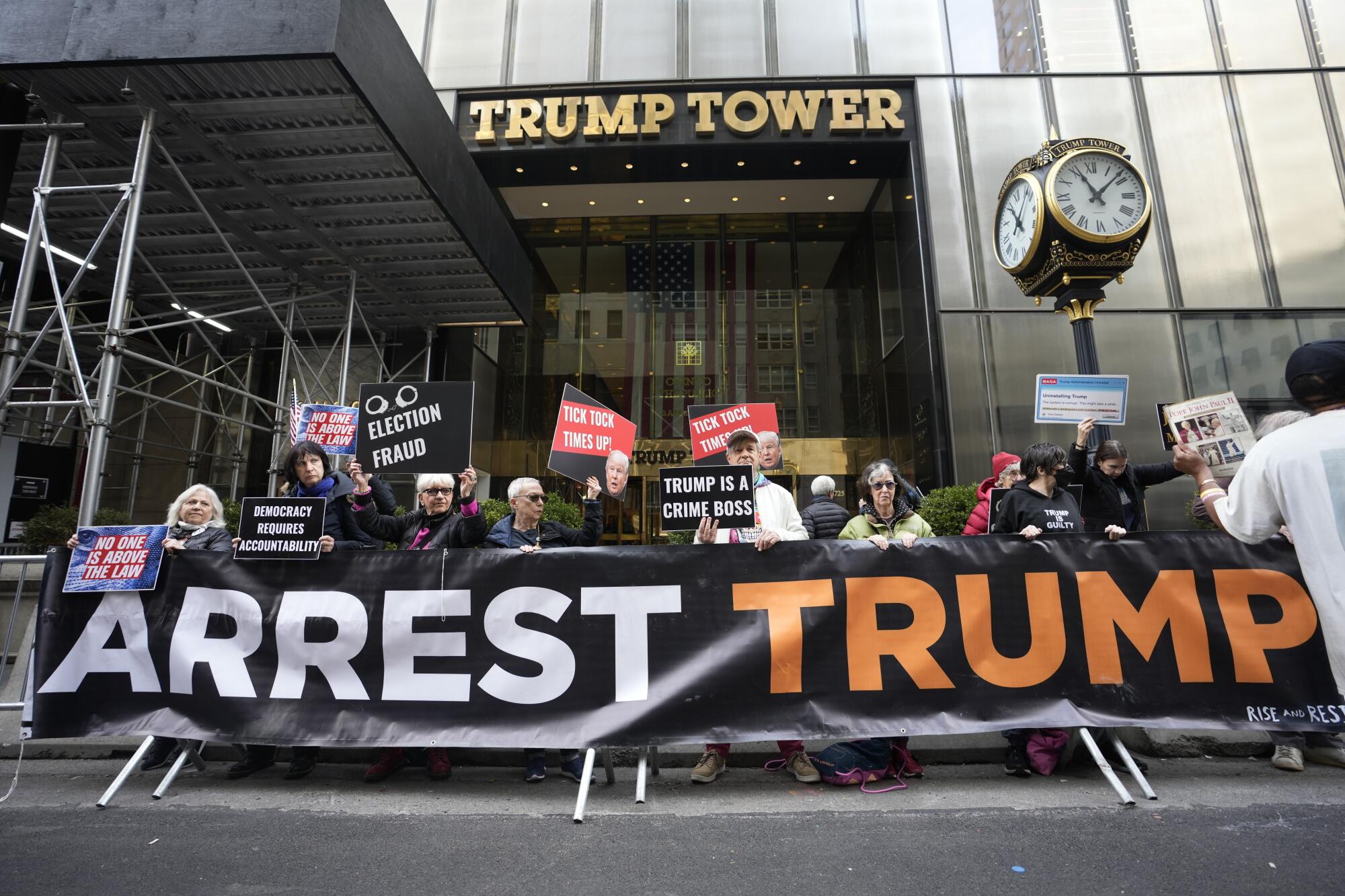 Protesters outside Trump Tower hold a large banner that reads, "Arrest Trump."