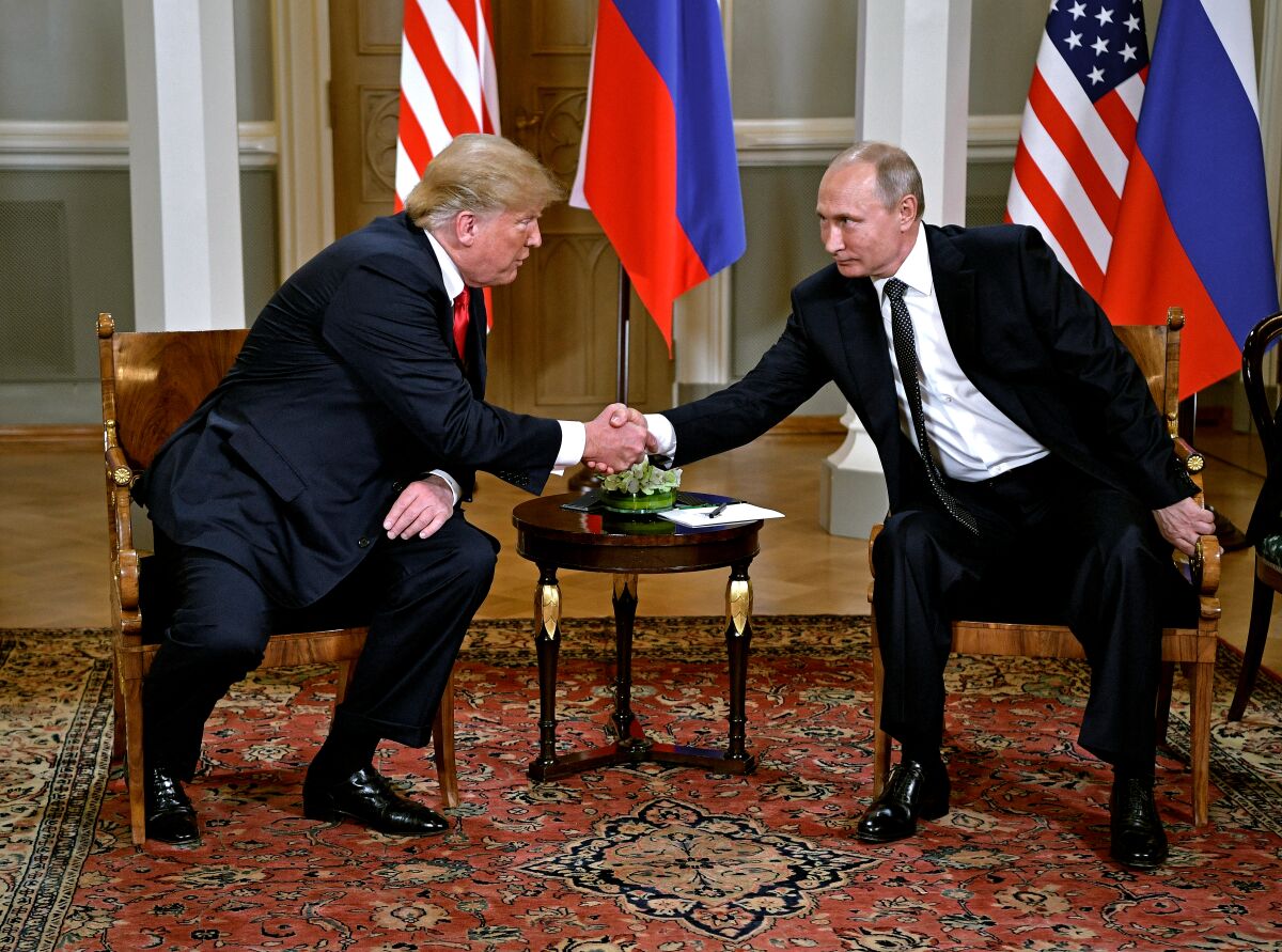 Former President Trump shakes hands with Vladimir Putin in 2018 with flags behind them.