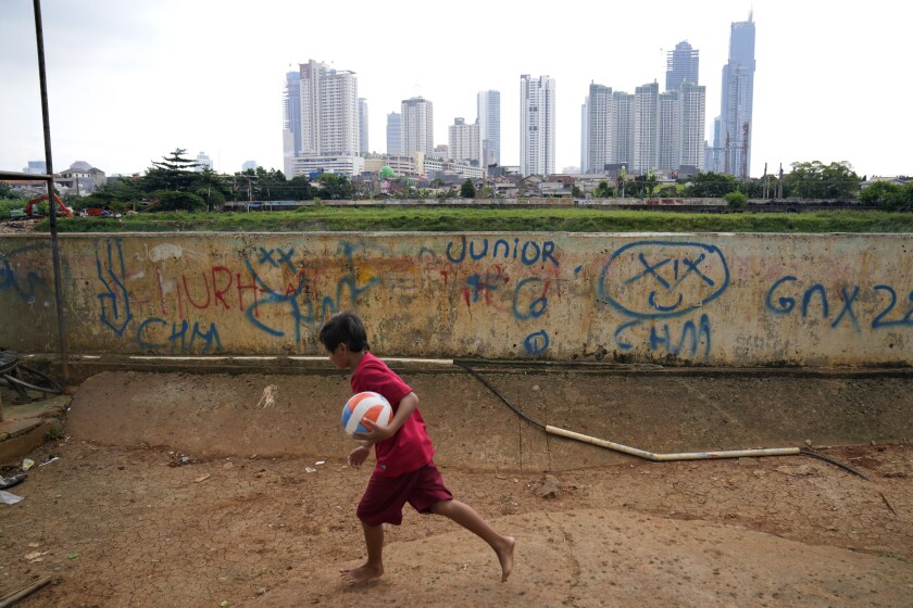 A young boy plays as high rise buildings at the main business district are seen in the background, in Jakarta, Indonesia, Tuesday, Jan. 25, 2022. Indonesian parliament last week passed the state capital bill into law, giving green light to President Joko Widodo to start a $34 billion construction project this year to move the country's capital from the traffic-clogged, polluted and rapidly sinking Jakarta on the main island of Java to jungle-clad Borneo island amid public skepticism. (AP Photo/Dita Alangkara)