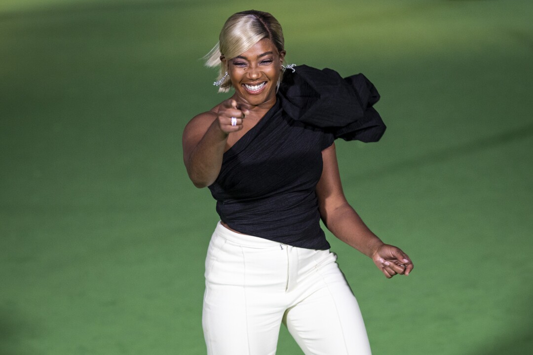 A woman pointing in a black shirt and white pants on a green carpet