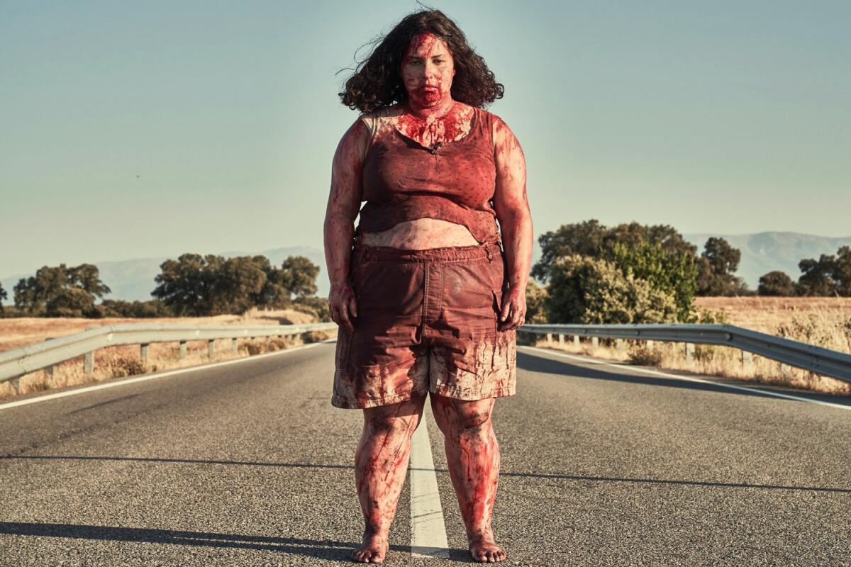 A bloodied woman stands in the middle of a rural highway