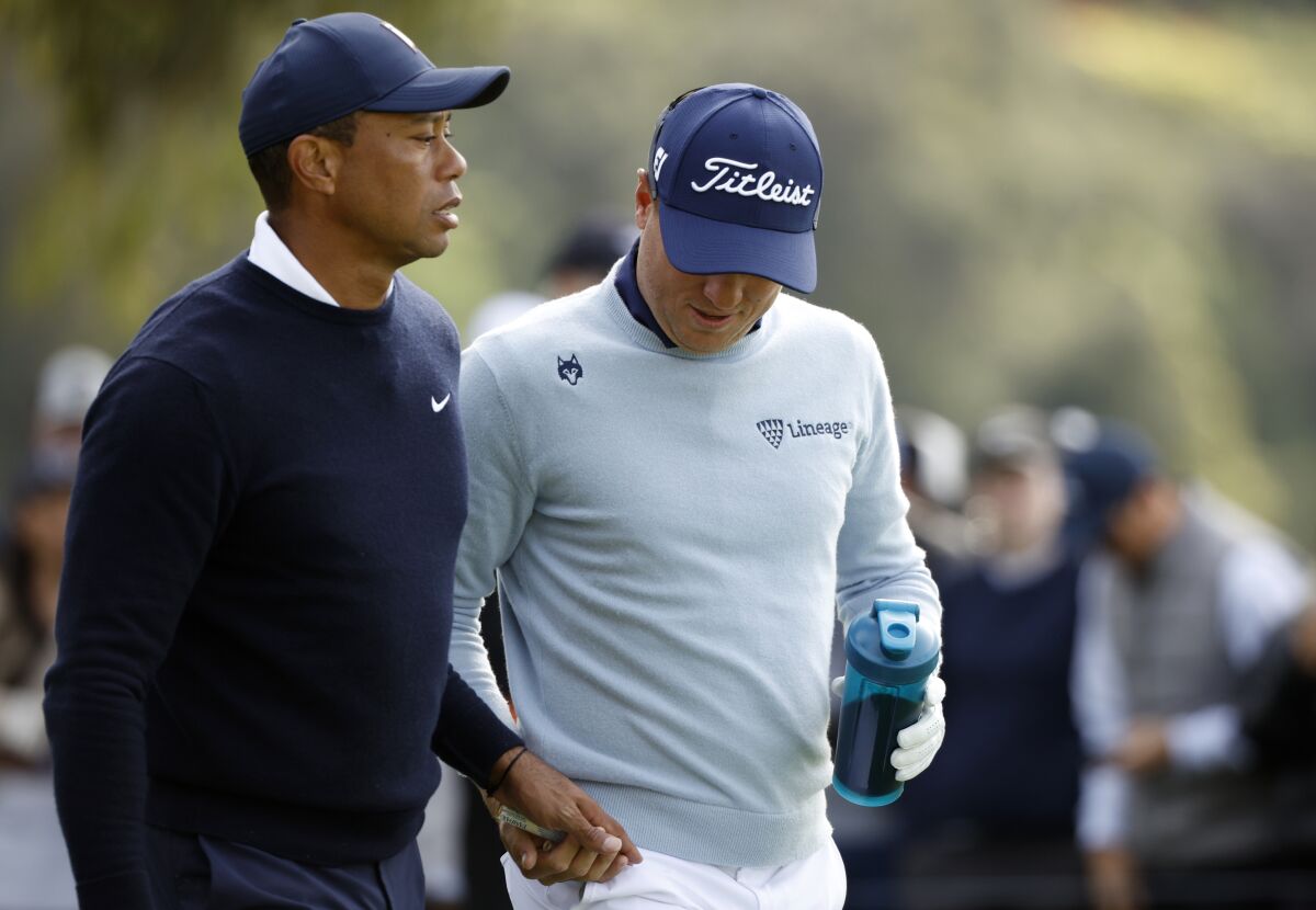 Tiger Woods, left, hands a tampon to Justin Thomas while walking away from the ninth tee.