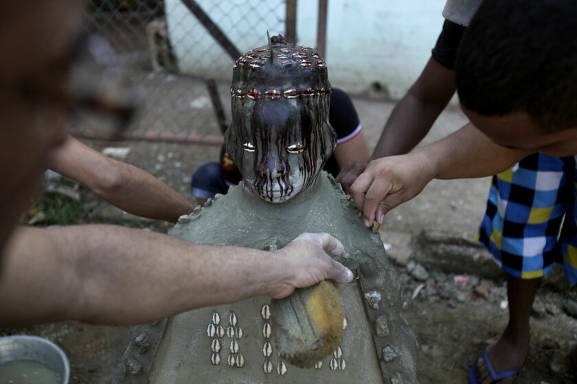 Santeria priests or babalawo add the finishing touches to the Eshu-Elegbara statue, on the eve of a New Year's ceremony at the Cuatro Caminos market in Havana, Cuba, Sunday, Dec. 29, 2013. Cubans gathered Monday in Havana's most important market to give thanks for the year’s blessings and ask for prosperity in 2014, singing ceremonial songs in the Yoruba language and spitting rum at the 2-foot-tall statue of Eshu-Elegbara, the deity associated with markets and commerce and also a protector of the universe. (AP Photo/Franklin Reyes)