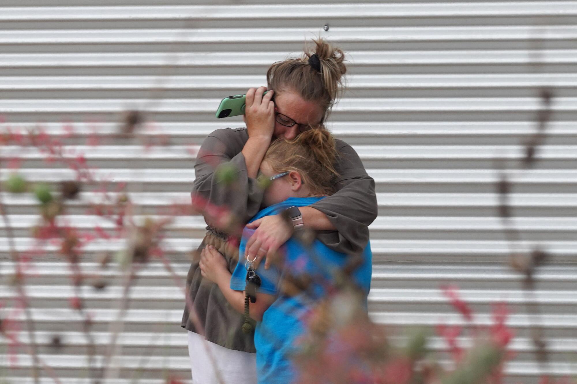 A woman cries and hugs a young girl while holding a phone 