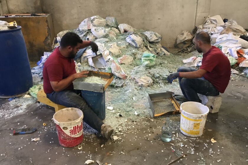 Two workers at a glassware factory in Tripoli sort through piles of blast-shattered glass.