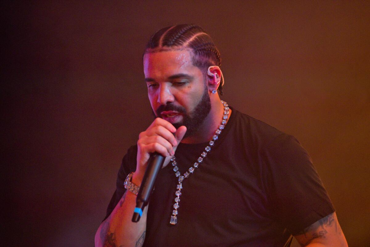 Drake performs with eyes down and a mic to his mouth while wearing a black T-shirt and diamond necklace