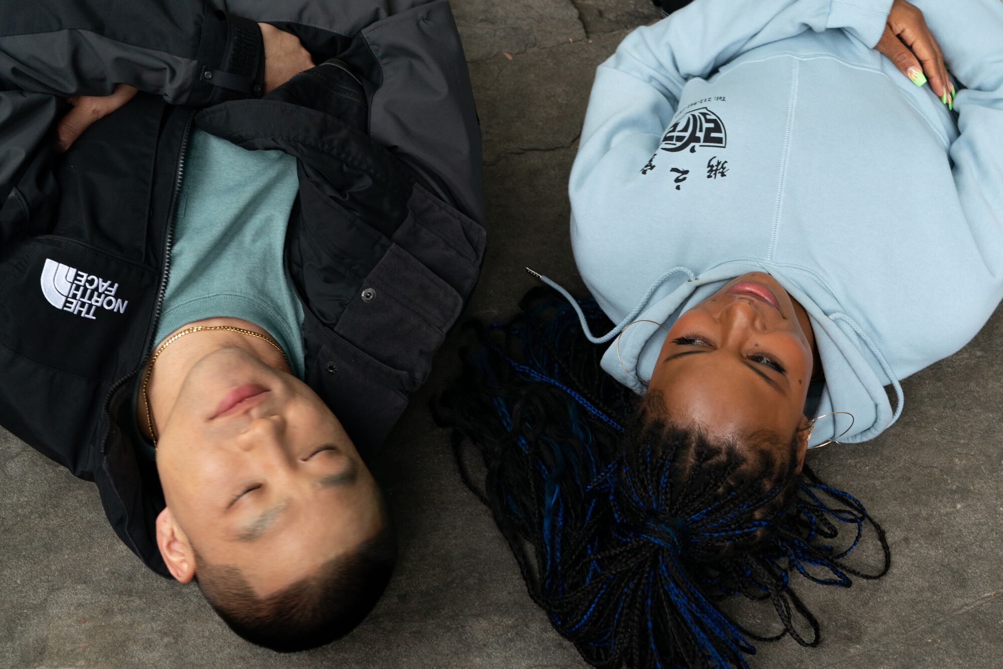 Taylor Takahashi lies on a floor, eyes closed, alongside Taylour Paige in a scene from the movie.