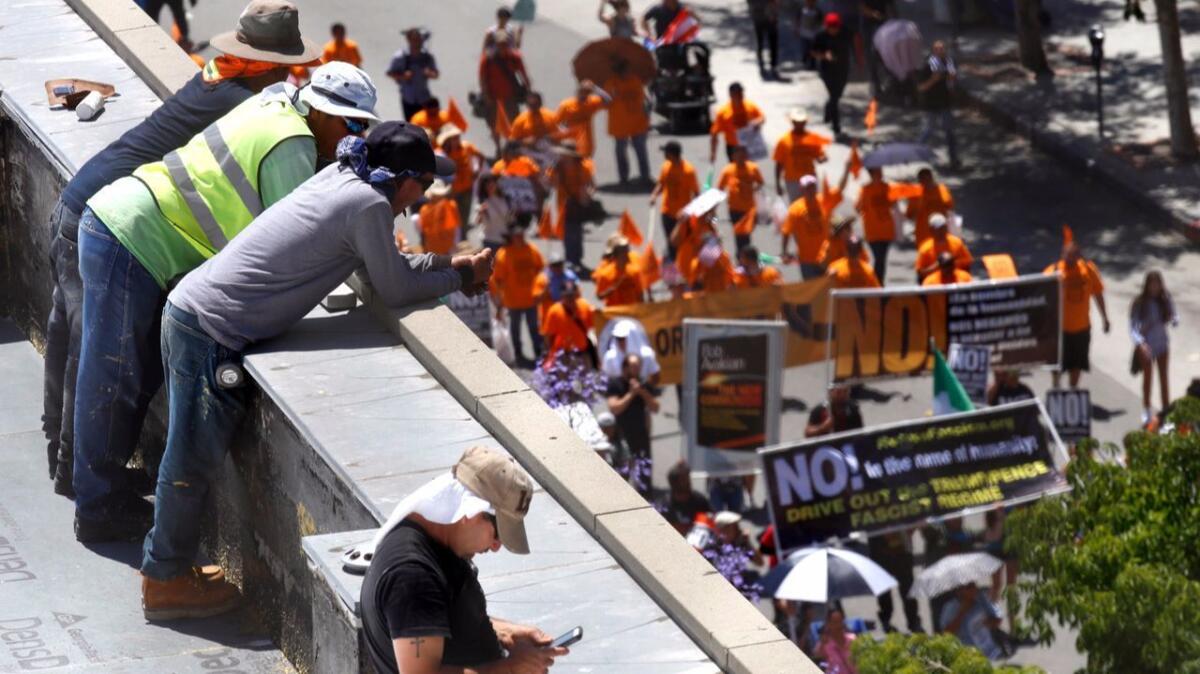 Workers take a break on a rooftop to watch a crowd of people marching on May Day. (Francine Orr / Los Angeles Times)