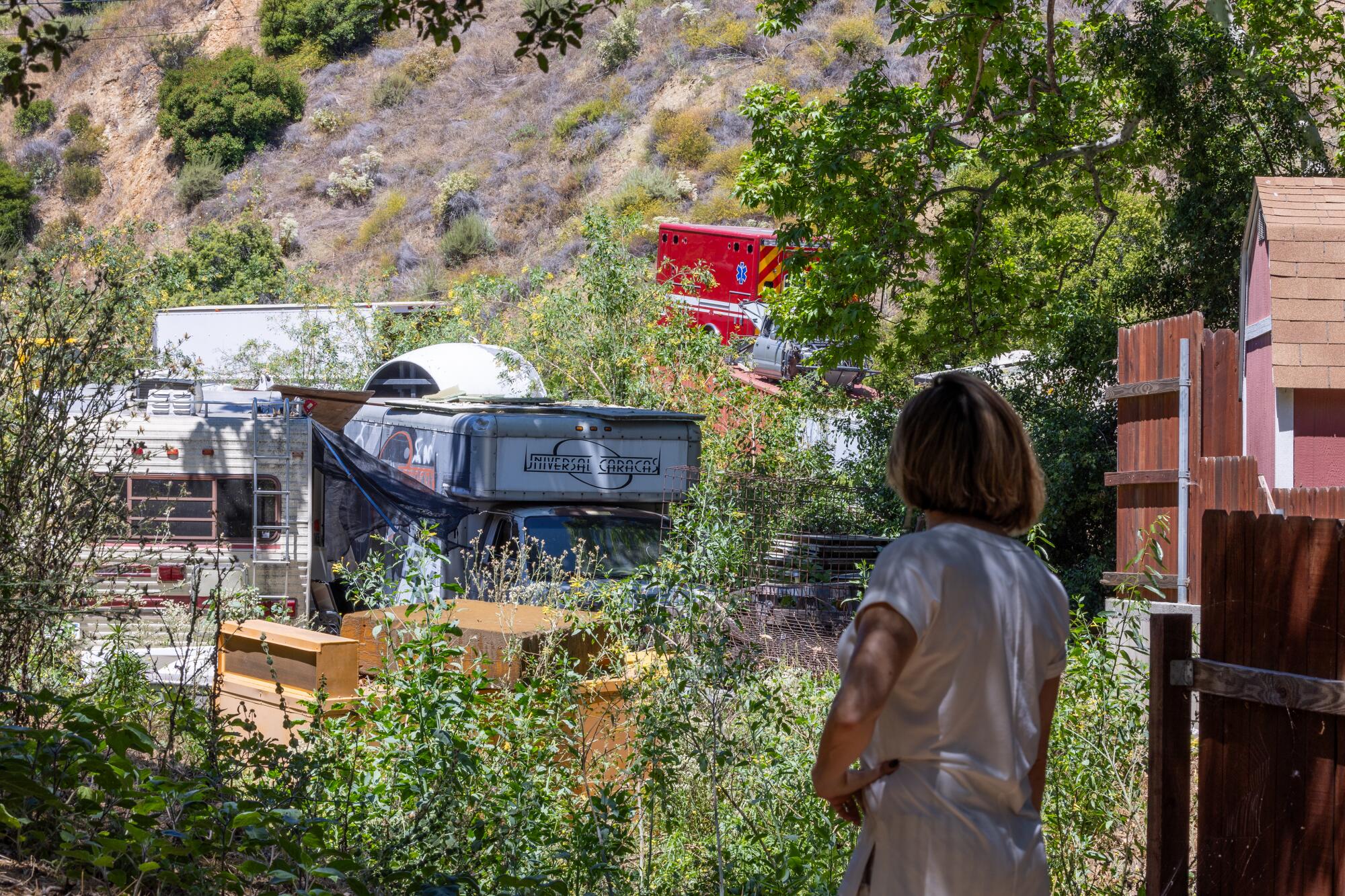  A woman looks at a neighboring property littered with vehicles and other objects. 