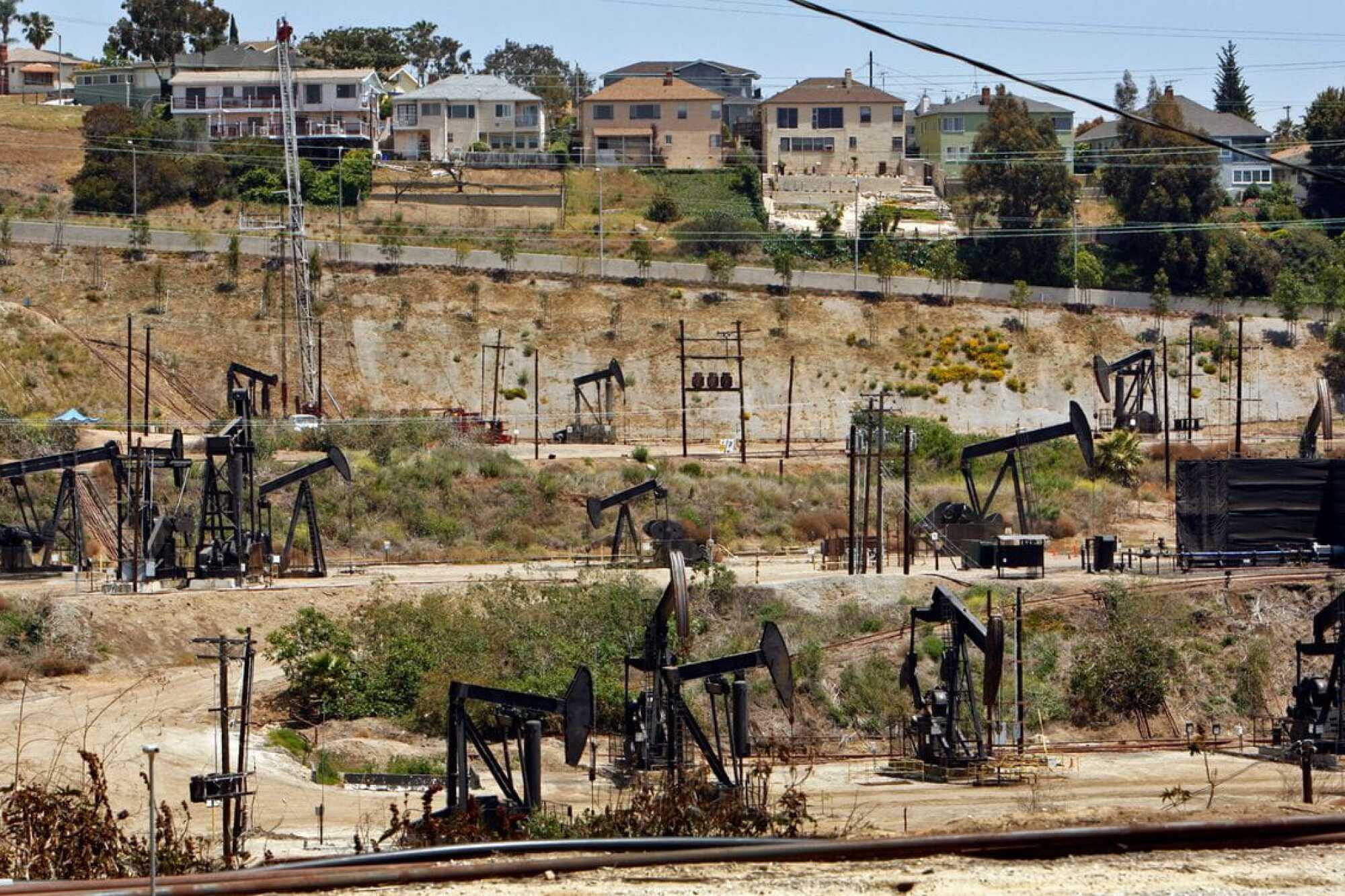 A residential community rises behind a field of oil pumpjacks.