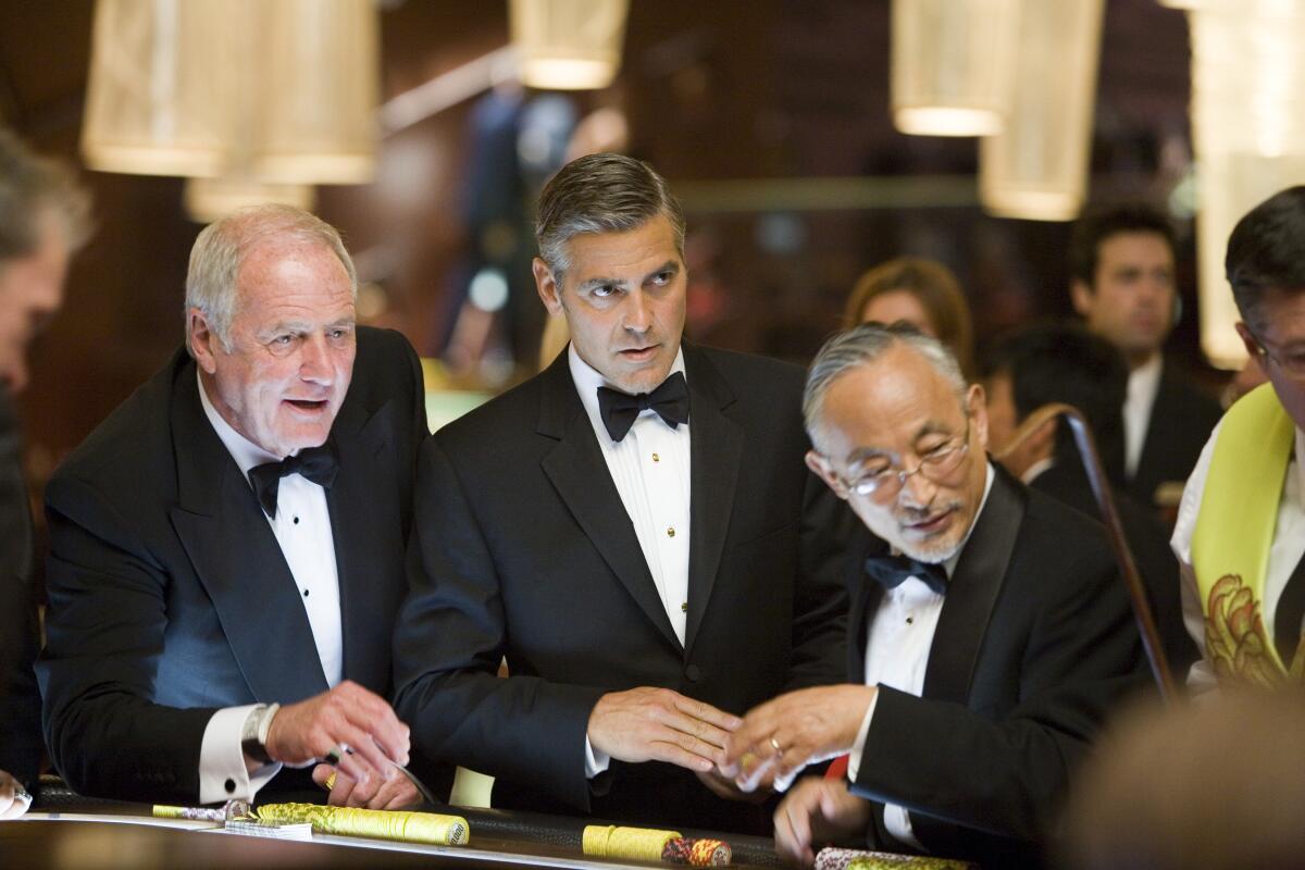 Three men in tuxedos stand at a casino table.