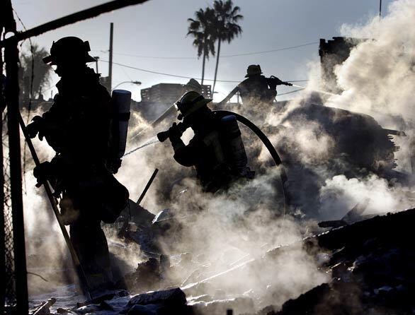 Los Angeles County firefighters extinguish a fire in a lot full of wooden pallets just north of the Century Freeway in unincorporated Willowbrook. The large smoke plume created a distraction for morning commuters on the freeway.