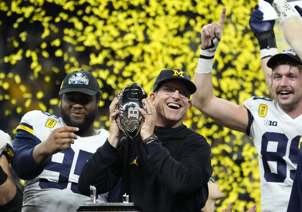  Jim Harbaugh holds a trophy surrounded by smiling players.