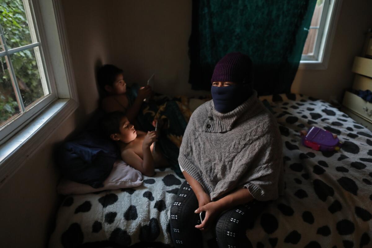 Odilia Leon wears a mask sitting on her bed with two of her children using electronic tablets