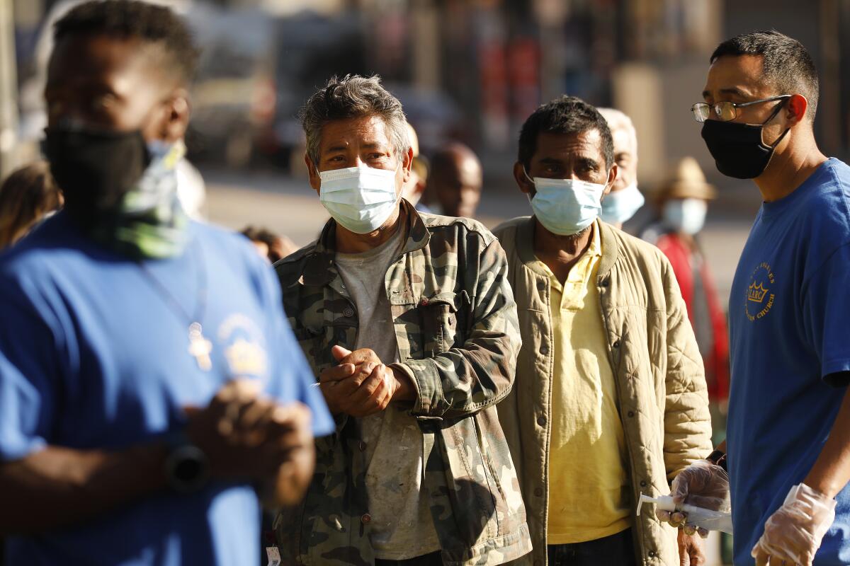 Mario Ynostrosa, right, with Los Angeles Restoration Church, gives hand sanitizer to people waiting in line for food.