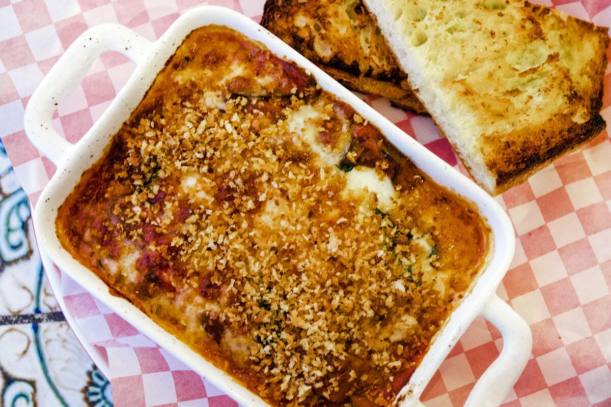 A baked pasta dish in a rectangular white dish with garlic bread on the side