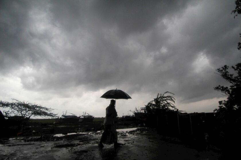 A villager holds an umbrella as dark clouds loom over Balasore district in Odisha, India, Tuesday, May 25, 2021.