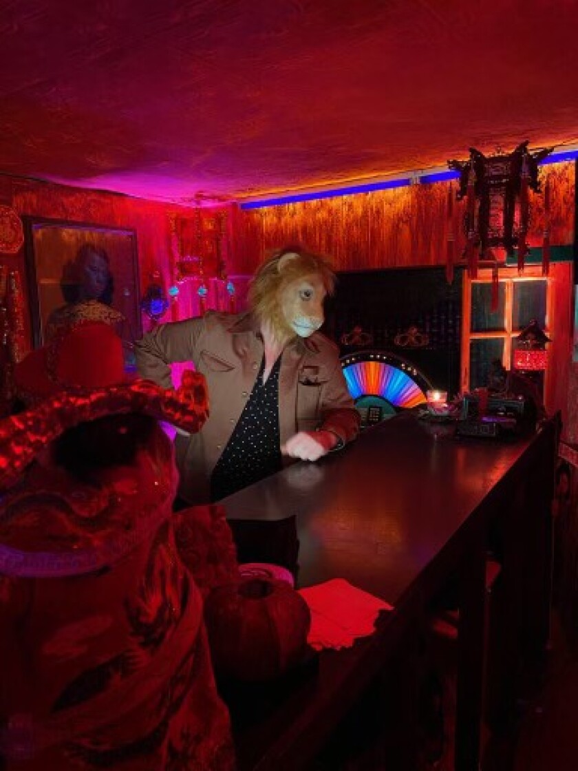 A guy wearing a lion head mask stands at the bar of a red-lit club.