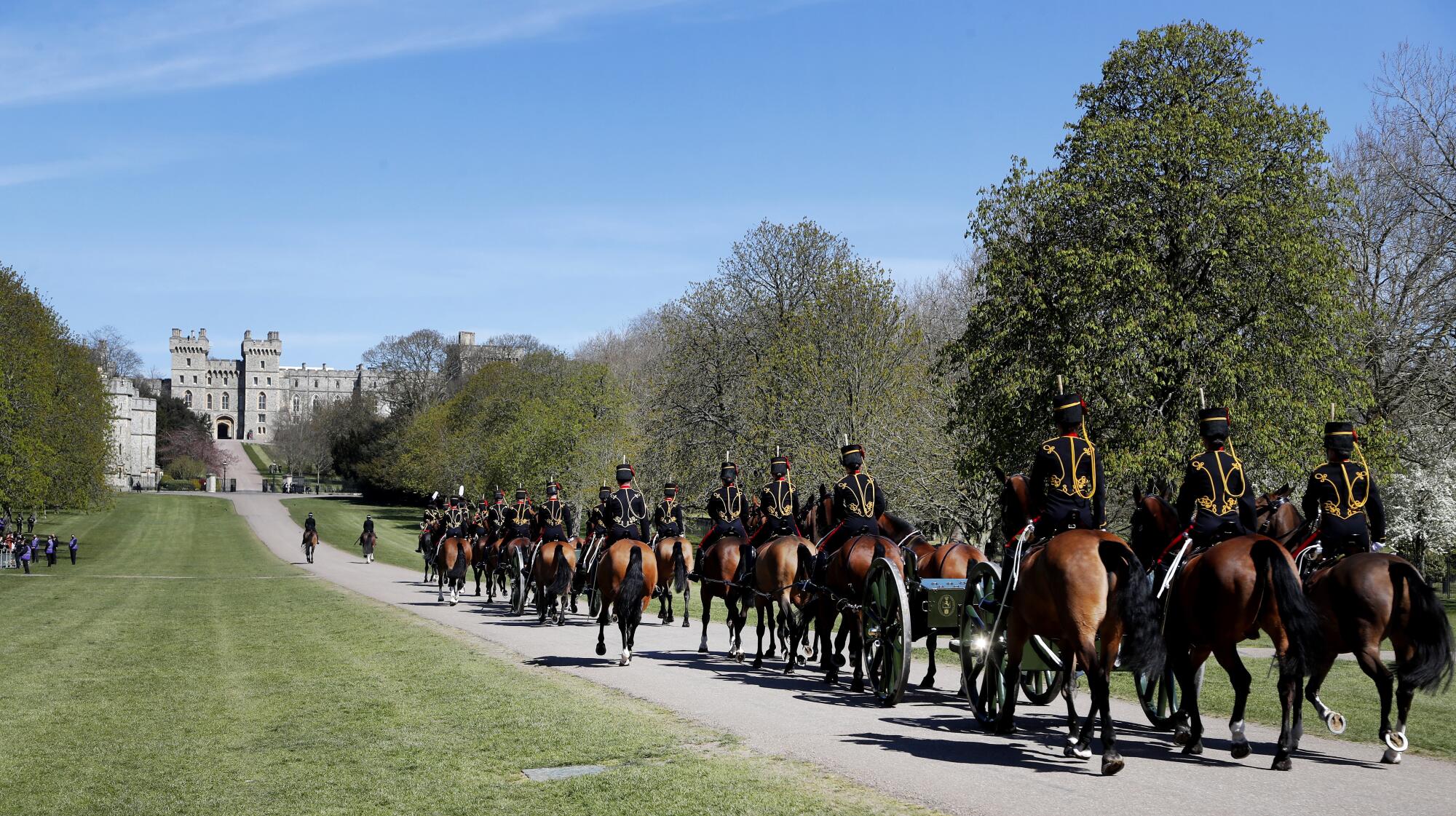 The King's Troop Royal Horse Artillery rides on a road toward Windsor Castle past trees and grass.