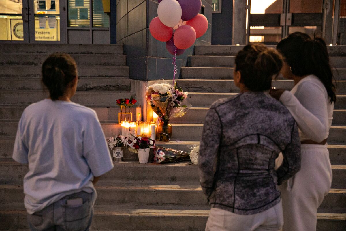 Three people standing at a vigil on the steps of a high school