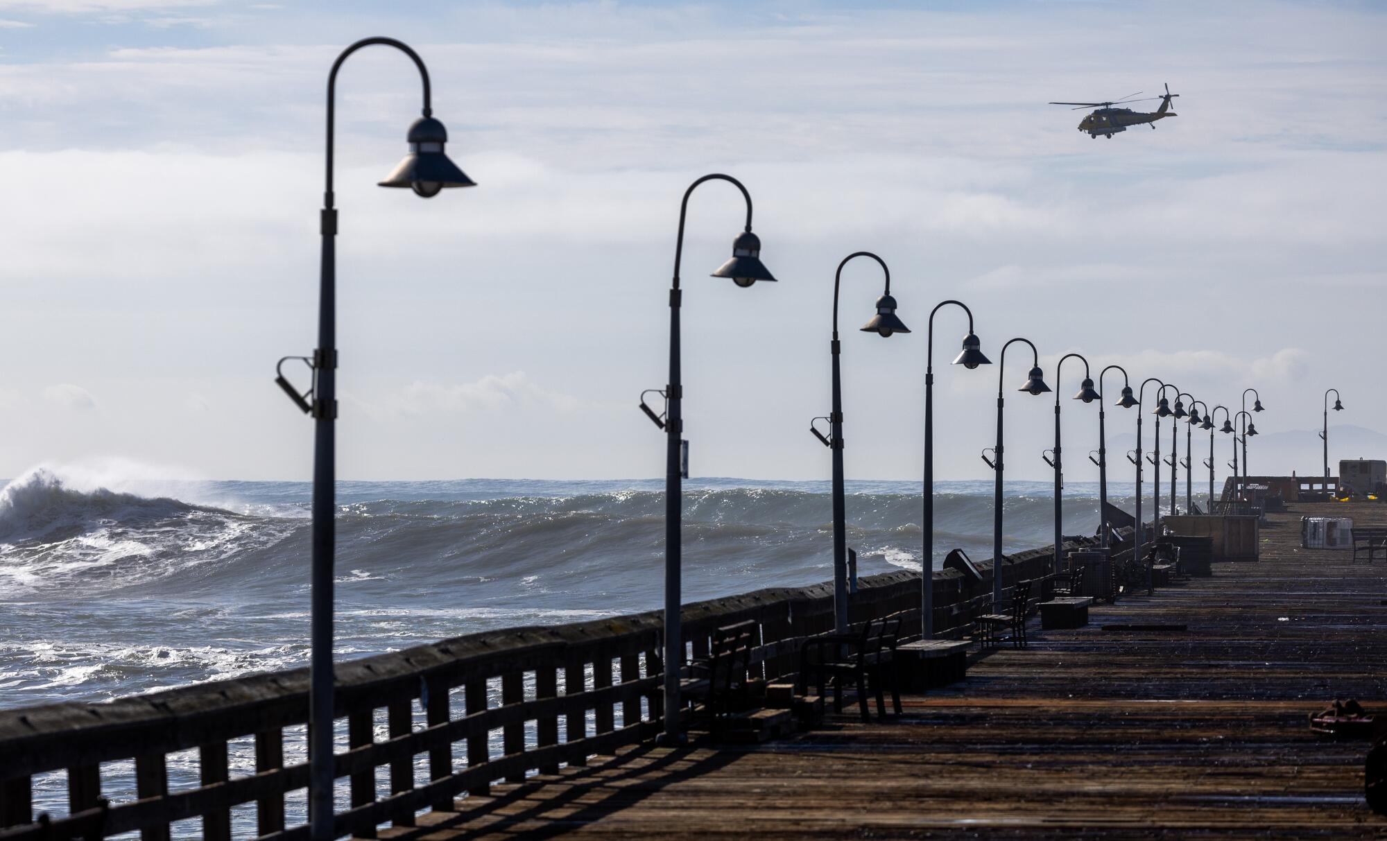 A helicopter flies above waves near a pier