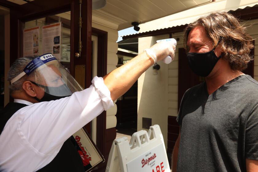 LOS ANGELES, CA - JULY 01, 2020 - - Waiter Pedro Armenta, wearing a face shield and mask, checks the temperature of customer Julian Bourely before entering Dupar's Restaurant which is still receiving customers for patio dining and take-out service at the Original Farmers Market in the Fairfax District in Los Angeles on July 1, 2020. All customers have to wear masks and have their temperature read before being allowed into the eatery. California Governor Gavin Newsom ordered indoor restaurants closed effective immediately on July 1, 2020. (Genaro Molina / Los Angeles Times)
