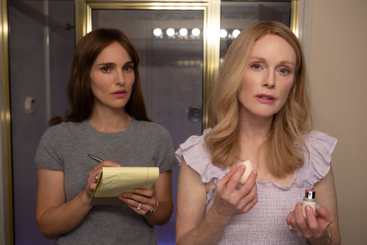 A woman with a notebook stands next to a woman applying makeup.