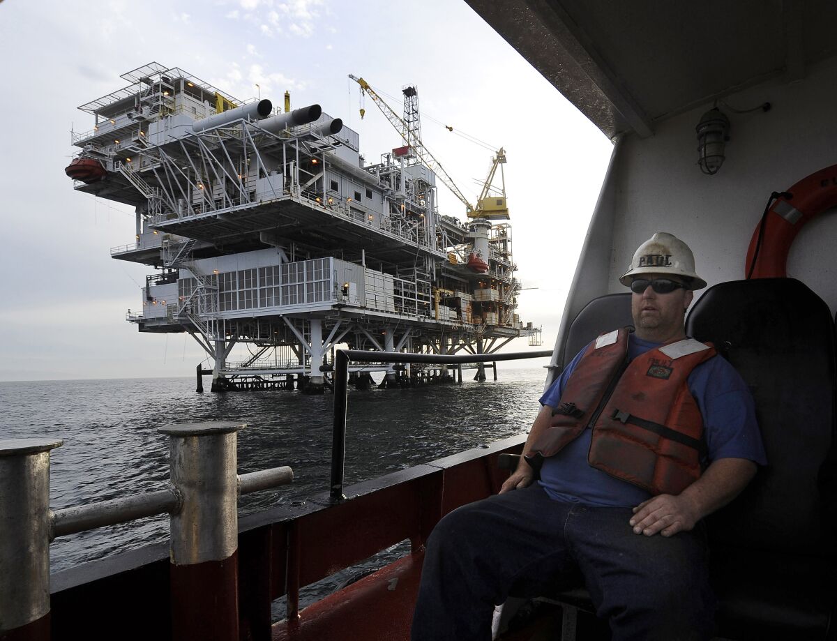 A worker in a hard hat arrives by boat at an offshore oil drilling platform.