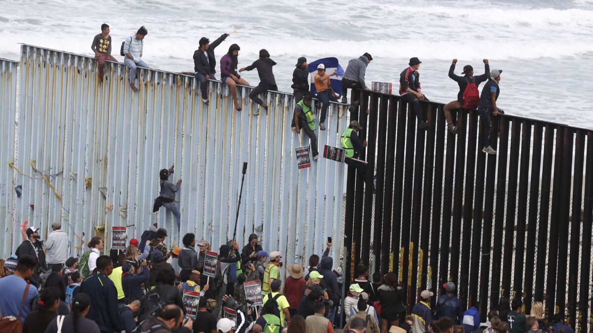 Immigrants and their supporters climb the border fencing in Playas de Tijuana.