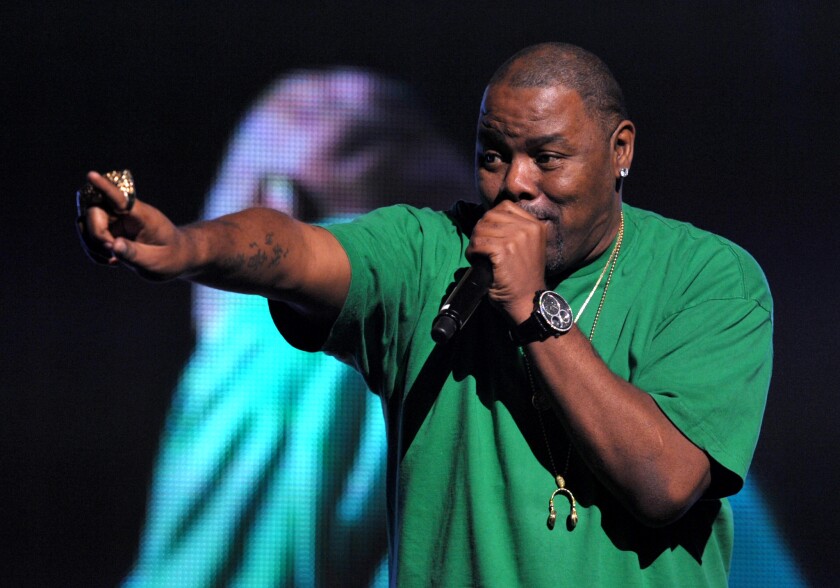 Biz Markie, onstage, holds a microphone to his mouth while pointing toward the audience with his other hand.
