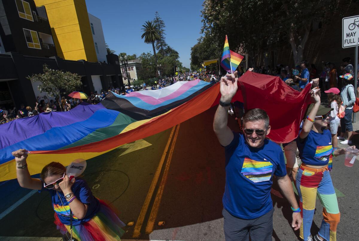 Participants in the OC Pride Parade carry an oversized Progress Pride flag 
