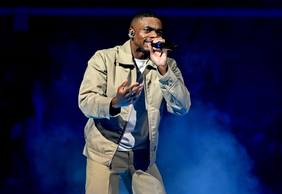 A man rapping onstage in tan pants and jacket