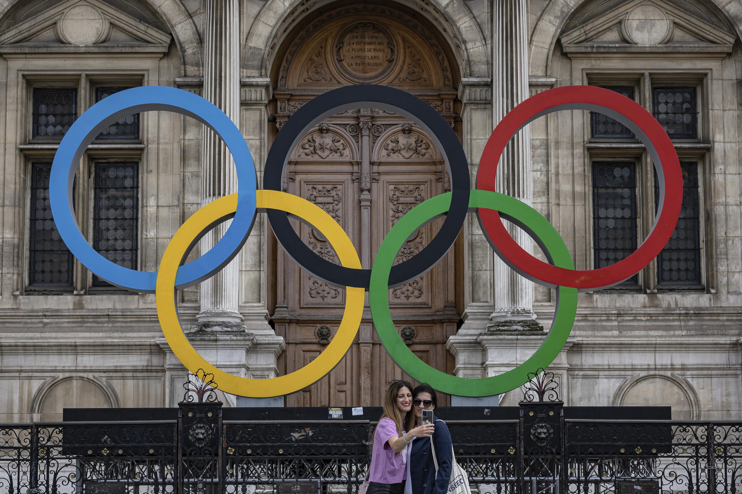 People take a photograph in front of the Olympic rings at Paris City Hall.