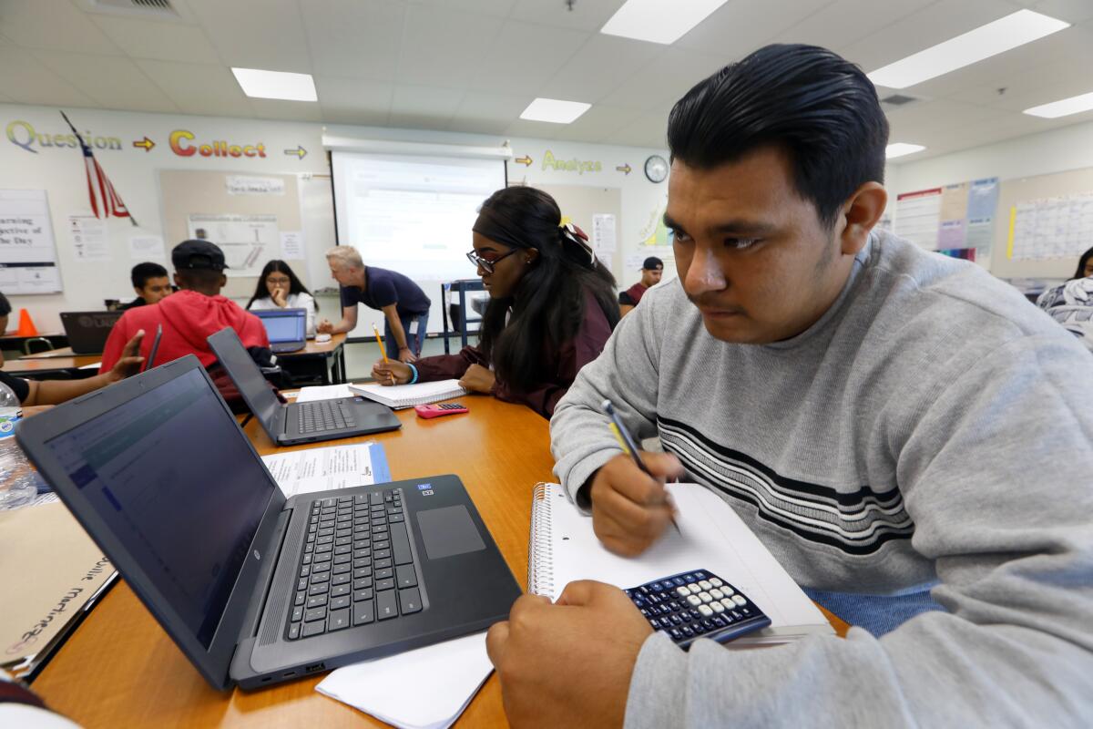 A high school senior looks at his laptop and takes notes 