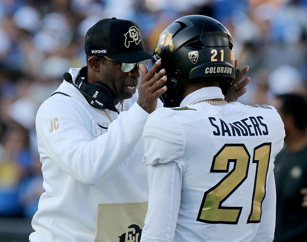 Colorado coach Deon Sanders talks with his son while holding both sides of his helmet at the Rose Bowl.