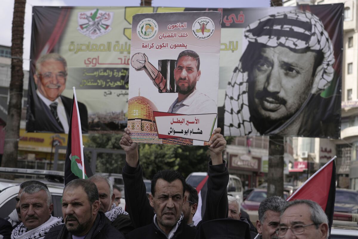 FILE - Palestinians attend a protest in solidarity with Hisham Abu Hawash, center, an Islamic Jihad member held by Israel under administrative detention, in the West Bank city of Ramallah, Jan, 2, 2022. HaMoked, an Israeli rights group that regularly gathers figures from prison authorities, said Monday, May 2, 2022, that as of May 2022, there were 604 detainees held in administrative detention, the highest number since 2016. The banner in Arabic reads, "Those starving behind bars feed the universe with dignity." (AP Photo/Majdi Mohammed, File)