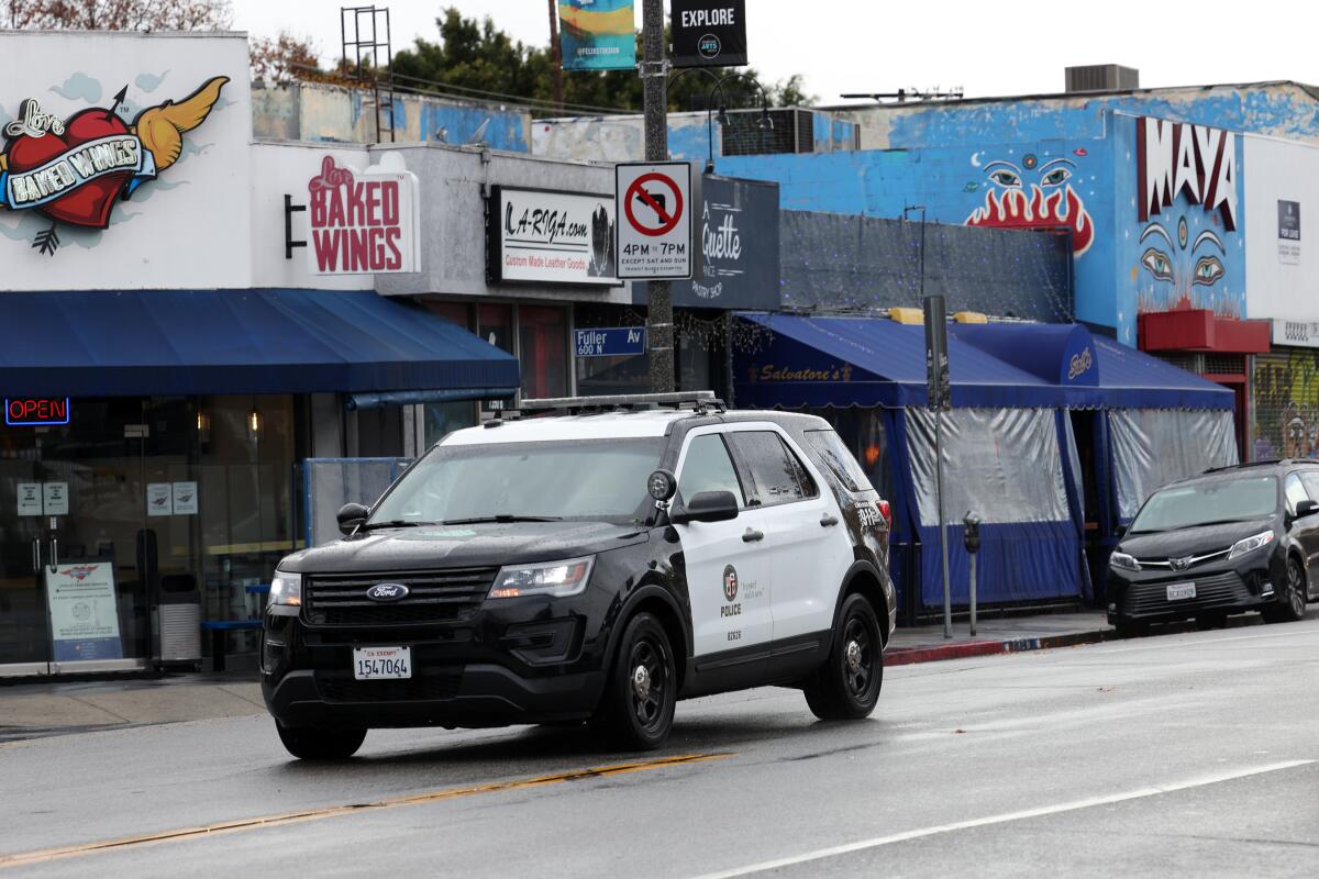 An LAPD patrol car rides along a street with stores