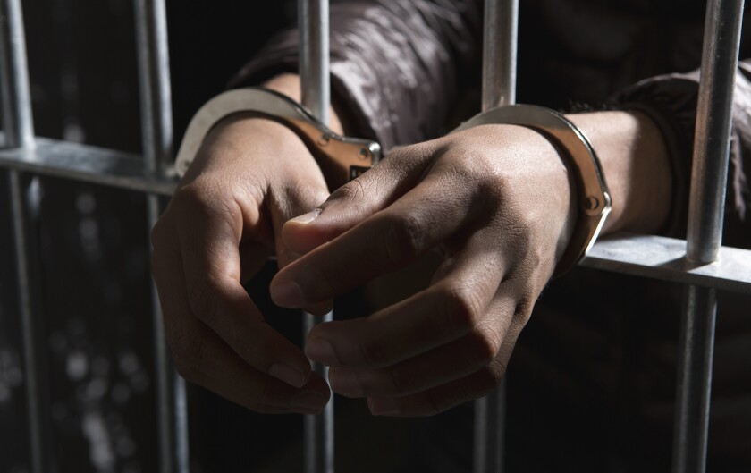 An inmate's hands cuffed in front of cell bars.